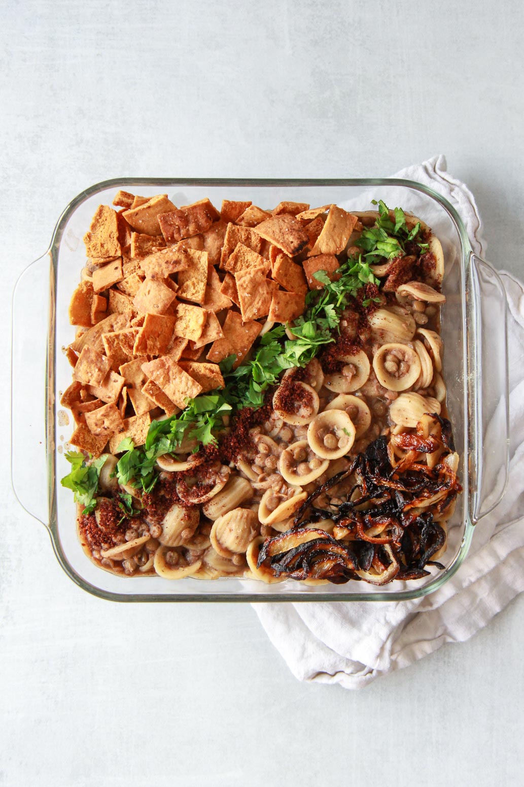 This Syrian pasta with lentils (horaa or horak osbao) is a great pantry friendly Middle Eastern comfort food. This vegan Mediterranean recipe is flavored with pomegranate molasses, sumac, and caramelized onions, and topped with crunchy pita chips.