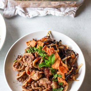 This Syrian pasta with lentils (horaa or horak osbao) is a great pantry friendly Middle Eastern comfort food. This vegan Mediterranean recipe is flavored with pomegranate molasses, sumac, and caramelized onions, and topped with crunchy pita chips.