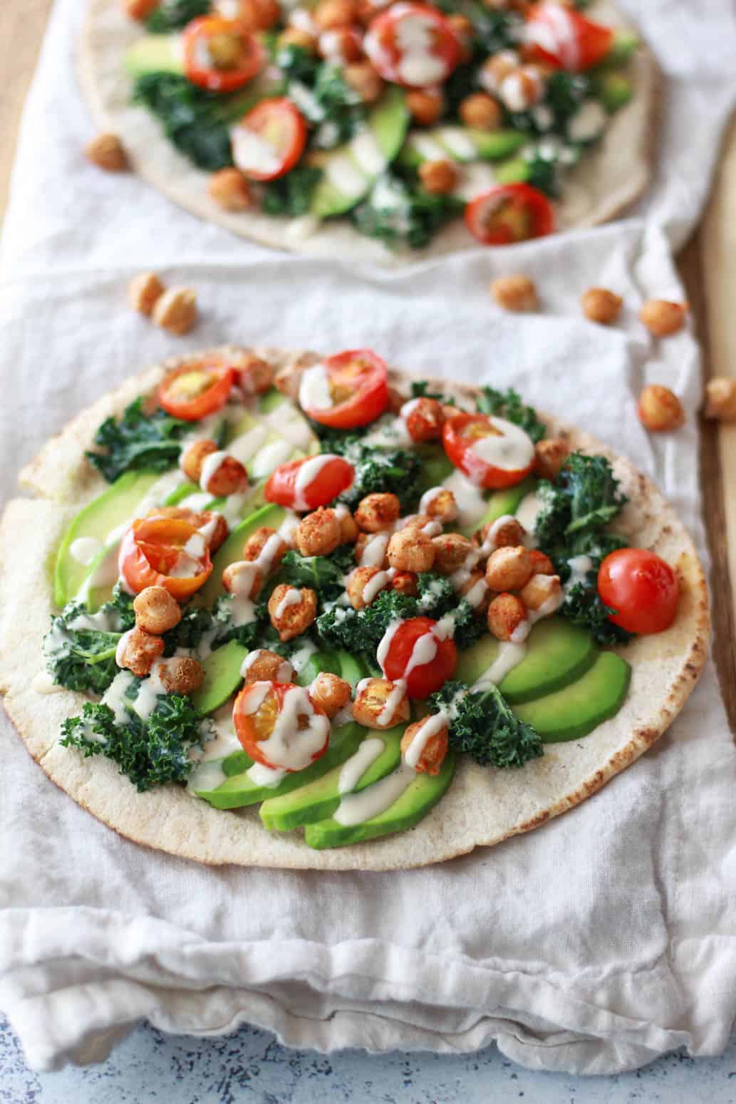 This avocado pita with spiced chickpeas and tahini puts a Mediterranean twist on avocado toast. This vegan recipe is topped with burst cherry tomatoes and massaged kale.