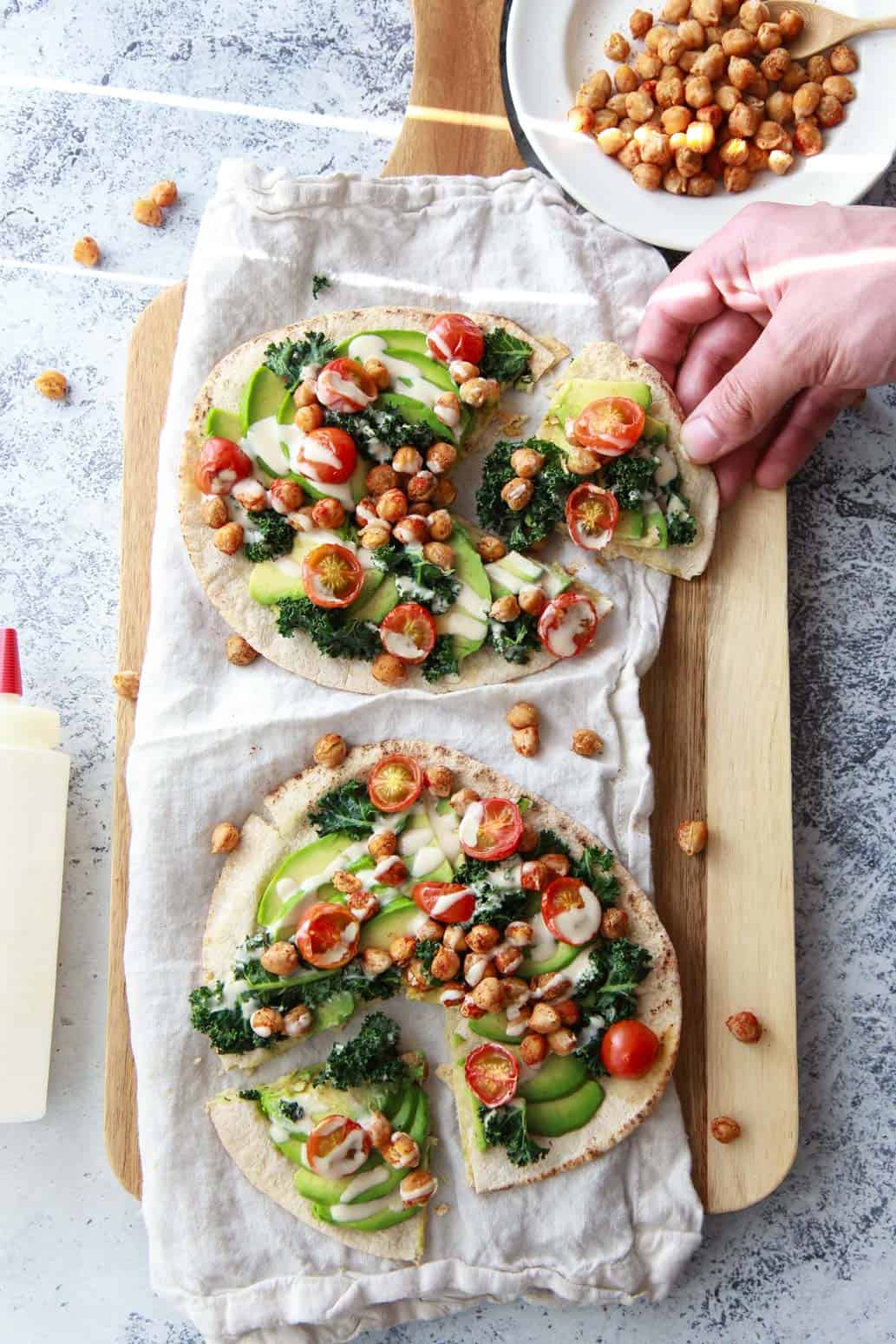 This avocado pita with spiced chickpeas and tahini puts a Mediterranean twist on avocado toast. This vegan recipe is topped with burst cherry tomatoes and massaged kale.