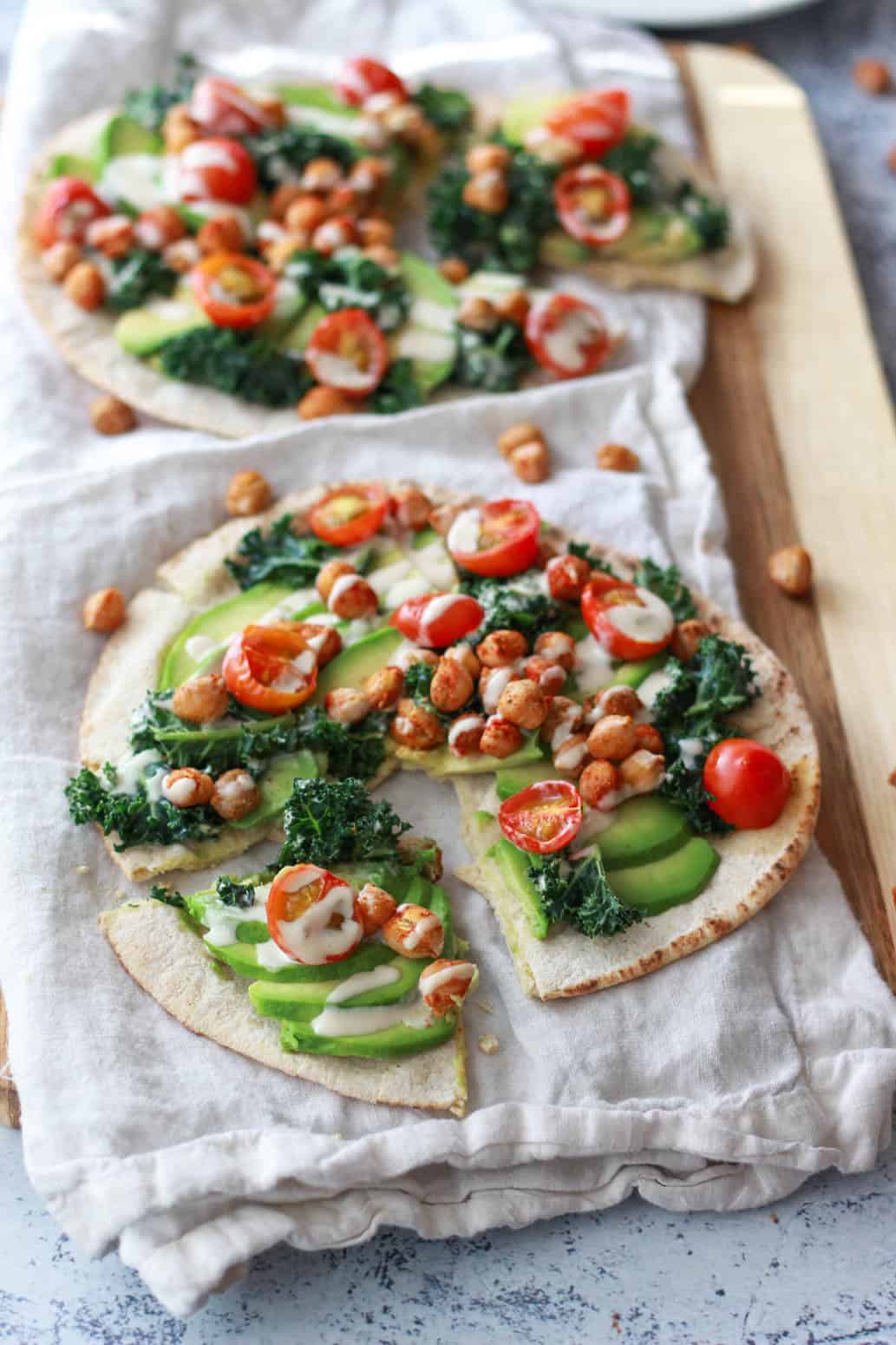 This avocado pita with spiced chickpeas and tahini puts a Mediterranean twist on avocado toast. This vegan recipe is topped with burst cherry tomatoes and massaged kale.