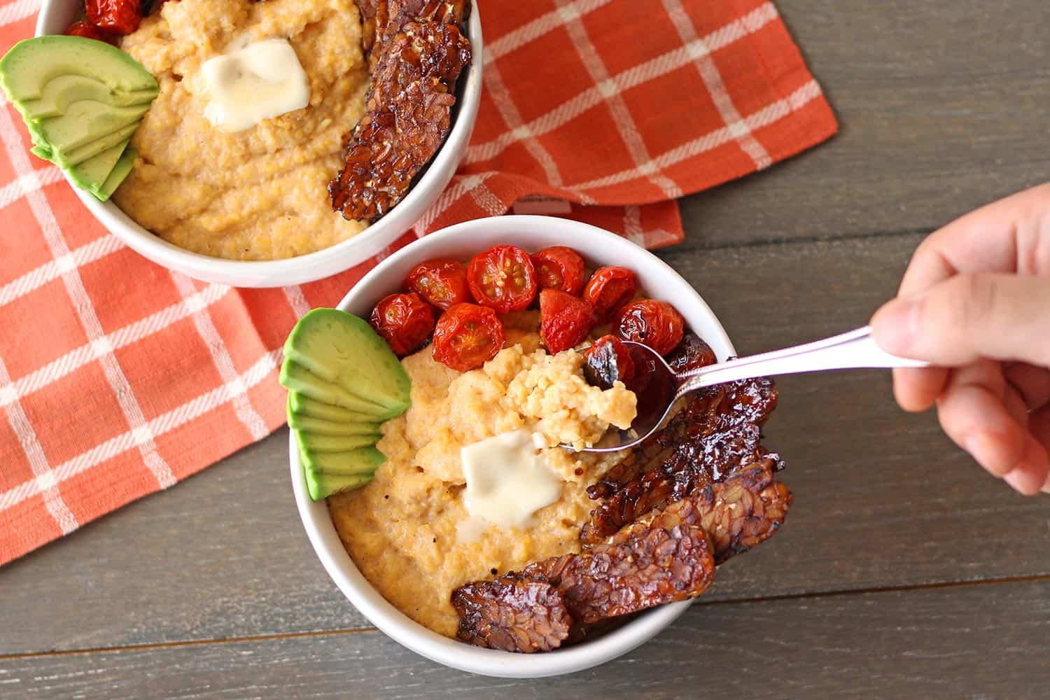 These creamy vegan grits are a delicious plant-based take on a Southern breakfast staple. Also gluten-free, these cheesy vegan grits recipe is topped with tempeh bacon and broiled tomatoes.