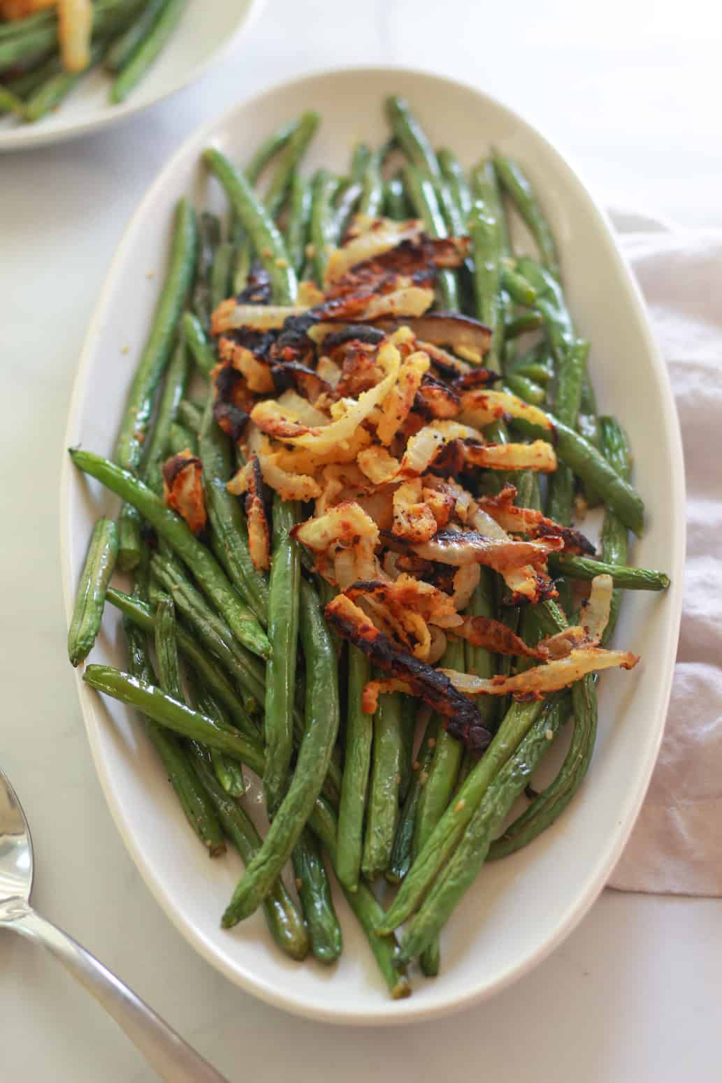 These lemon garlic green beans are simply roasted in the oven and topped with crispy chickpea fried onions. This is a simple vegan and gluten-free side dish recipe.