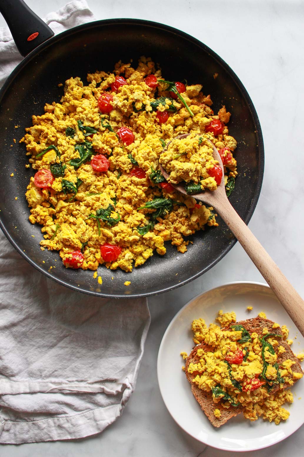 How to make a super flavorful tofu scramble with spinach and cherry tomatoes. Forget about “bland” tofu, this tofu scramble is bursting with umami flavor, seasoned with nutritional yeast and tahini. A great plant-based alternative to scrambled eggs, this flavorful tofu scramble recipe is sure to be a vegan breakfast favorite!
