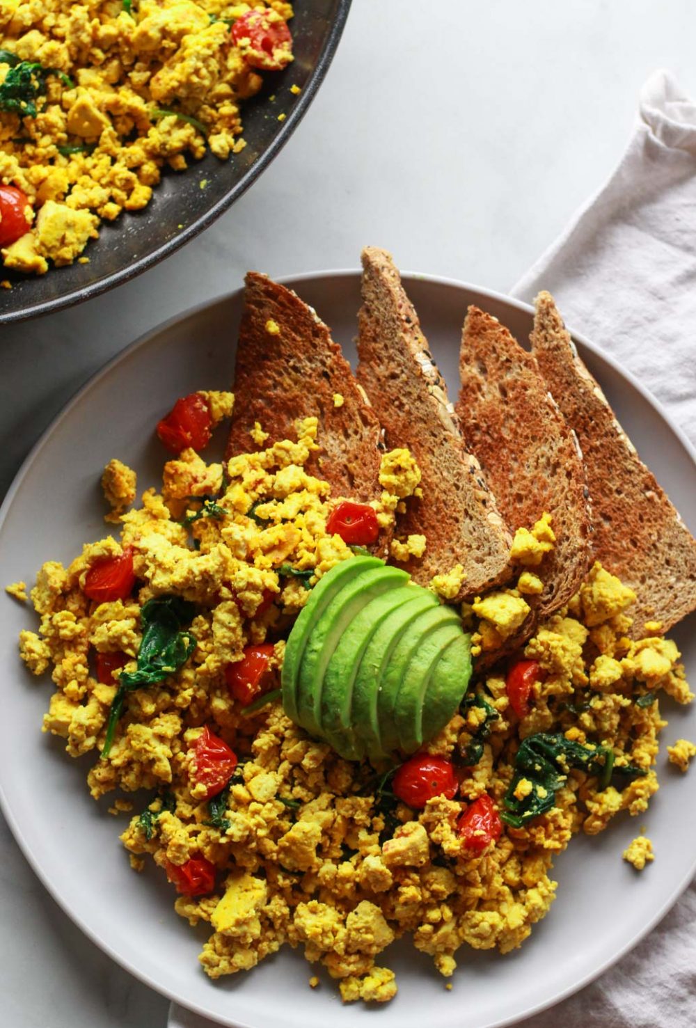 How to make a super flavorful tofu scramble with spinach and cherry tomatoes. Forget about “bland” tofu, this tofu scramble is bursting with umami flavor, seasoned with nutritional yeast and tahini. A great plant-based alternative to scrambled eggs, this flavorful tofu scramble recipe is sure to be a vegan breakfast favorite!