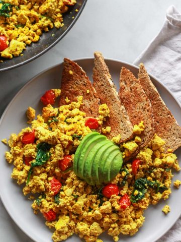 How to make a super flavorful tofu scramble with spinach and cherry tomatoes. Forget about “bland” tofu, this tofu scramble is bursting with umami flavor, seasoned with nutritional yeast and tahini. A great plant-based alternative to scrambled eggs, this flavorful tofu scramble recipe is sure to be a vegan breakfast favorite!