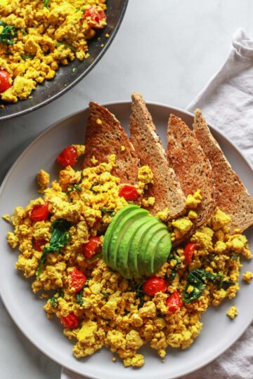 How to make a super flavorful tofu scramble with spinach and cherry tomatoes. Forget about “bland” tofu, this tofu scramble is bursting with umami flavor, seasoned with nutritional yeast and tahini. A great plant-based alternative to scrambled eggs, this flavorful tofu scramble recipe is sure to be a vegan breakfast favorite!