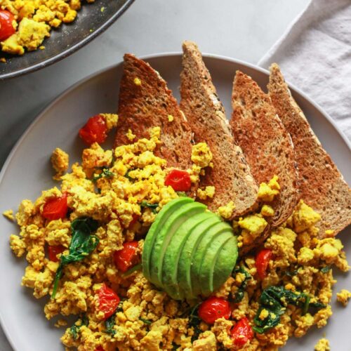 How to make a super flavorful tofu scramble with spinach and cherry tomatoes. Forget about “bland” tofu, this tofu scramble is bursting with umami flavor, seasoned with nutritional yeast and tahini. A great plant-based alternative to scrambled eggs, this flavorful tofu scramble recipe is sure to be a vegan breakfast favorite!