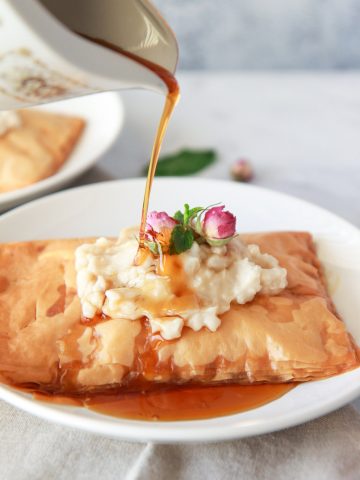 This vegan Kahi with Geymar is an Iraqi pastry with a thick oat cream, topped with date syrup. This pastry is made up of layers of flaky phyllo dough, topped with vegan clotted cream, called Qaymar. Topped with date syrup or honey for a non-vegan option, this dessert is irresistible.