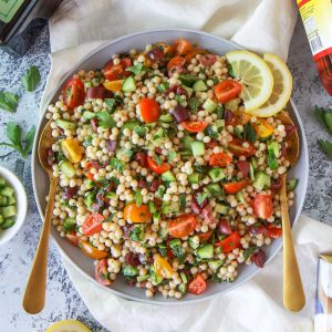 Mediterranean pearl couscous salad featuring moghrabieh couscous, lemon, cucumber, and olives, in a lemon herb olive oil dressing.