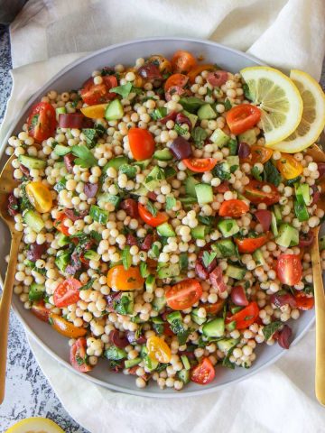 Mediterranean pearl couscous salad featuring moghrabieh couscous, lemon, cucumber, and olives, in a lemon herb olive oil dressing.