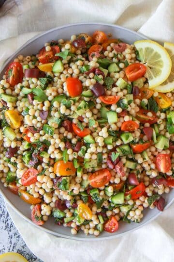 Mediterranean pearl couscous salad featuring moghrabieh couscous, lemon, cucumber, and olives, in a lemon herb olive oil dressing.