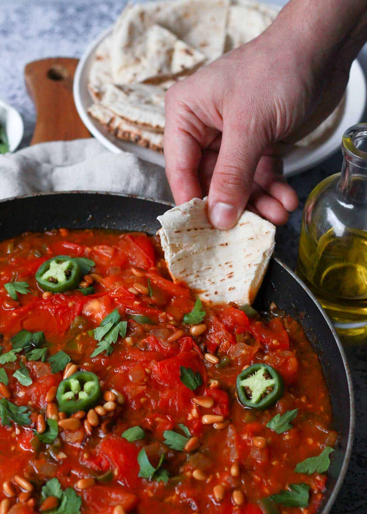 This is an image of dipping pita bread into the galayet bandora, pan fried tomatoes dish.