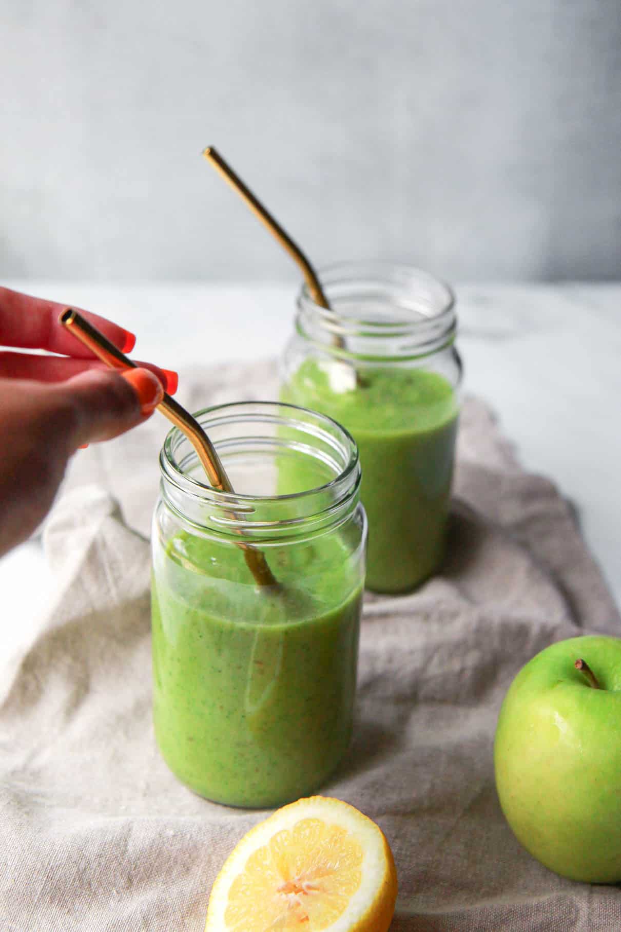 Hand holding the straw of the green apple smoothie