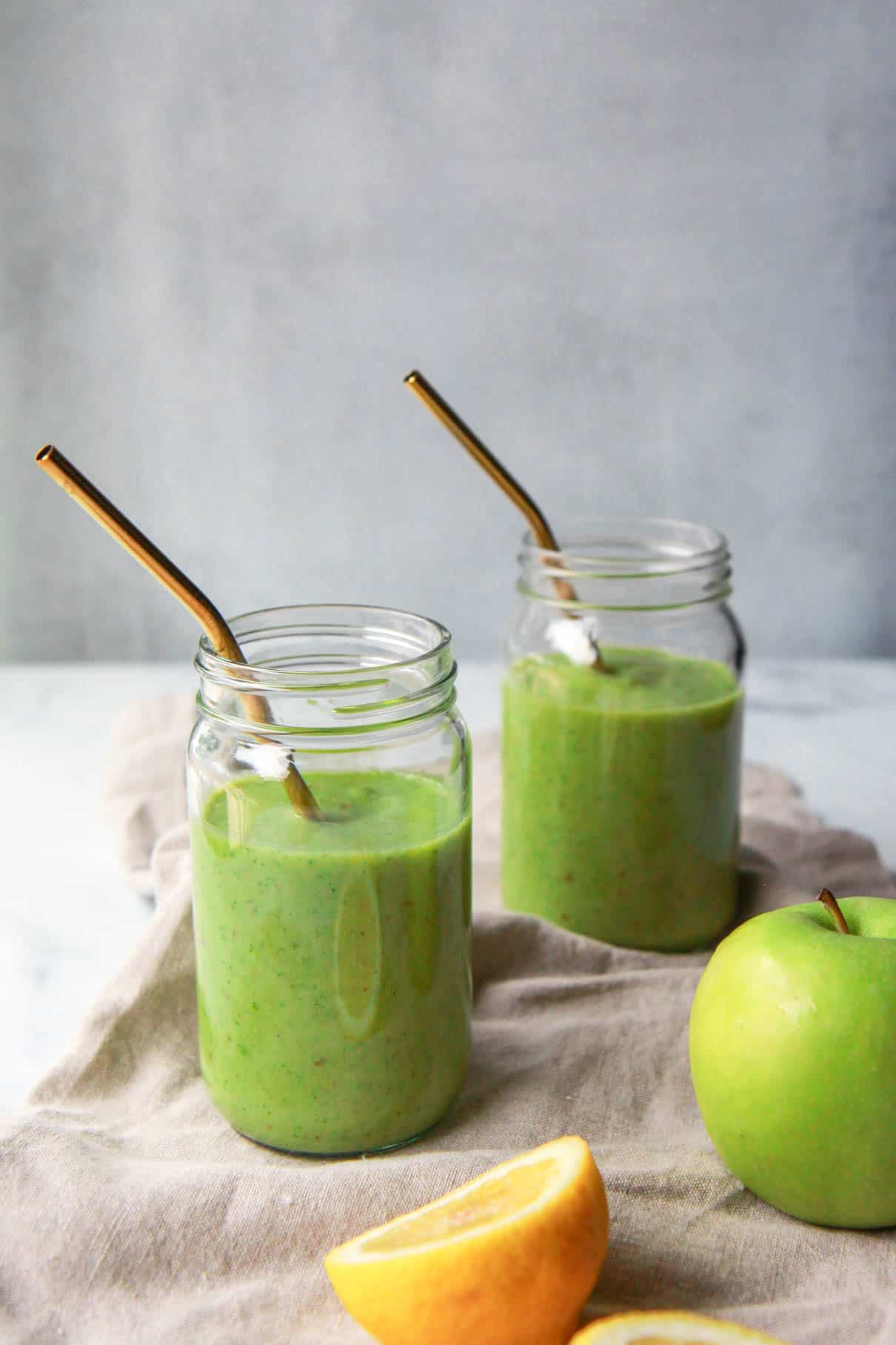 a zoomed out view of the two kale apple smoothie jars, lemon, and green apple