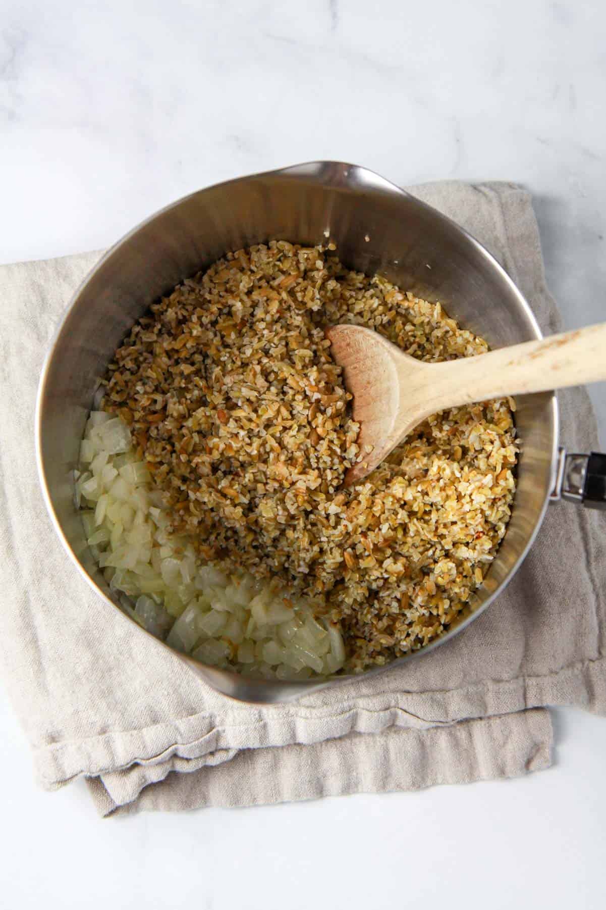 The rinsed freekeh is being added to the pot of sautéed onions.