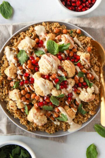 The freekeh recipe shown with the cooked freekeh, topped with roasted cauliflower and chickpeas and drizzled with tahini.