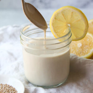 Lemon tahini sauce being drizzled with a spoon to show consistency.