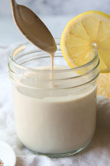 Lemon tahini sauce being drizzled with a spoon to show consistency.