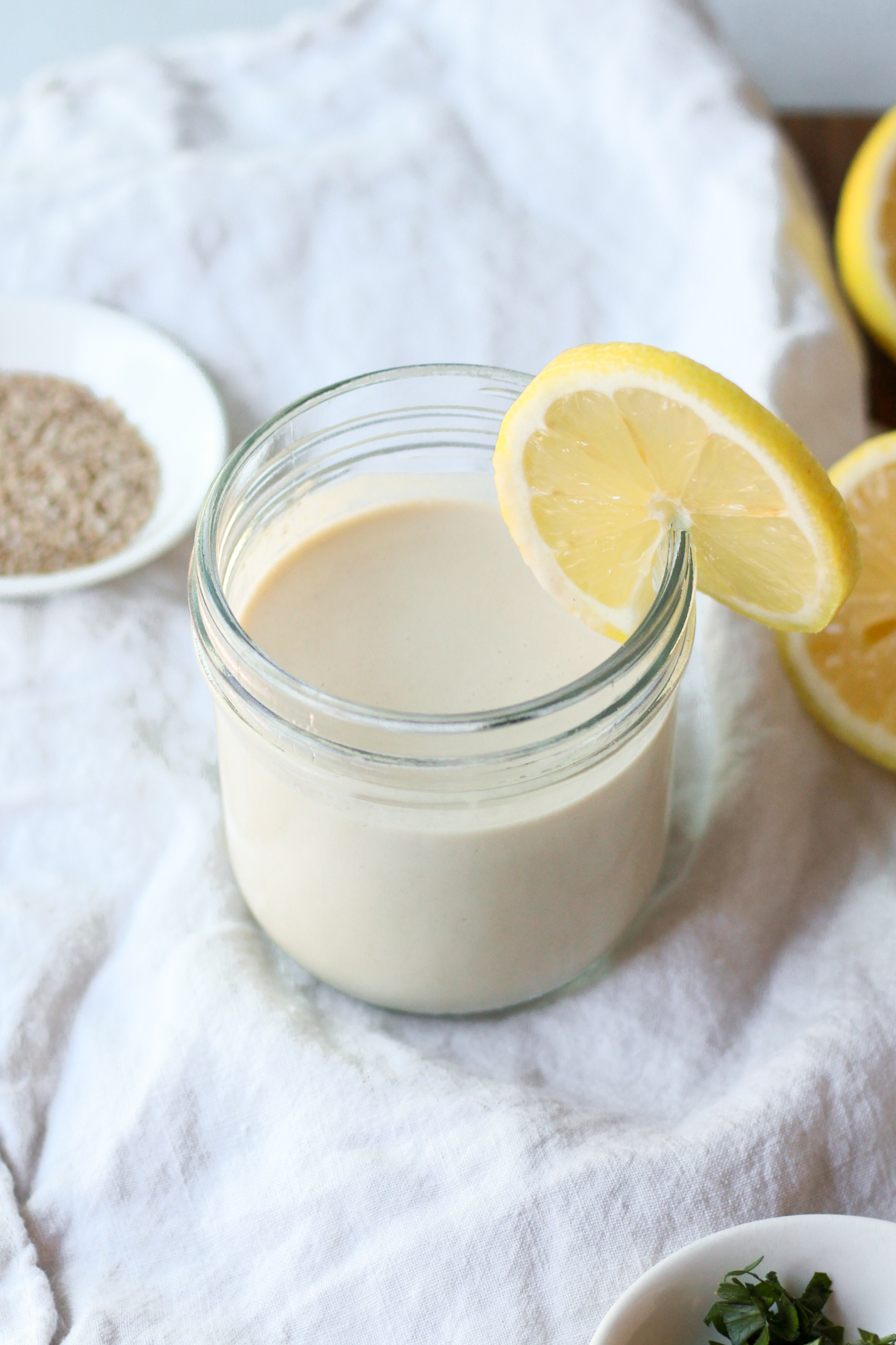 Lemon tahini sauce being stored in a jar garnished with a lemon.