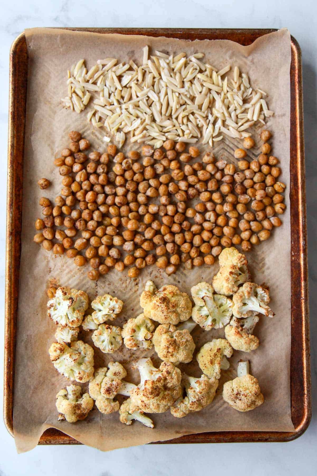 The almonds, tossed with olive oil, are added to the baking tray of roasted cauliflower and chickpeas.