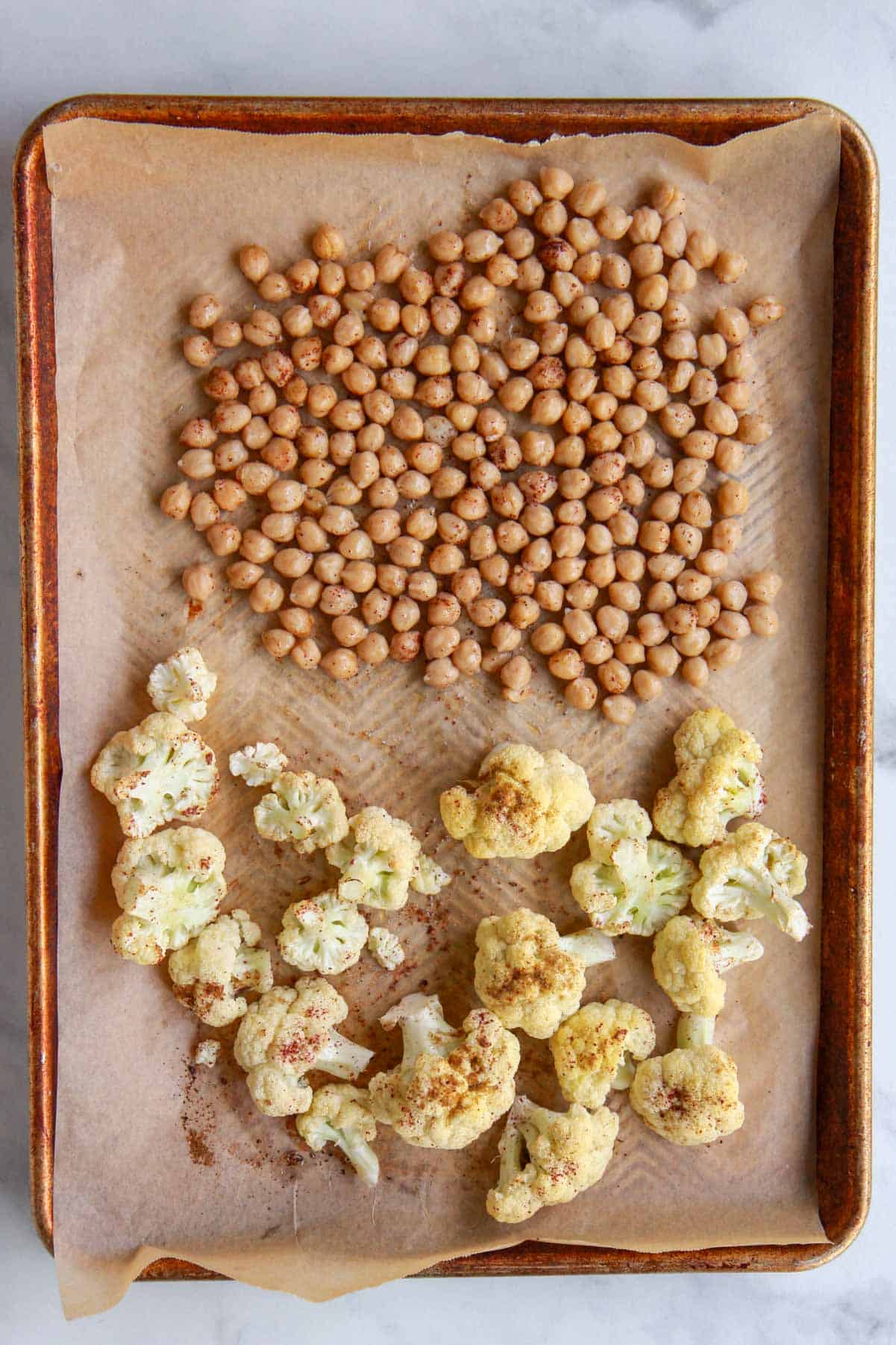 The chickpeas, tossed with olive oil and spices, are added to the baking tray with roasted cauliflower.