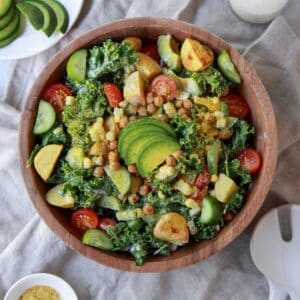 Finished image of the kale salad topped with tahini dressing, chickpeas, and slices of avocado.