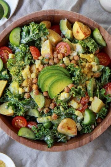 Finished image of the kale salad topped with tahini dressing, chickpeas, and slices of avocado.