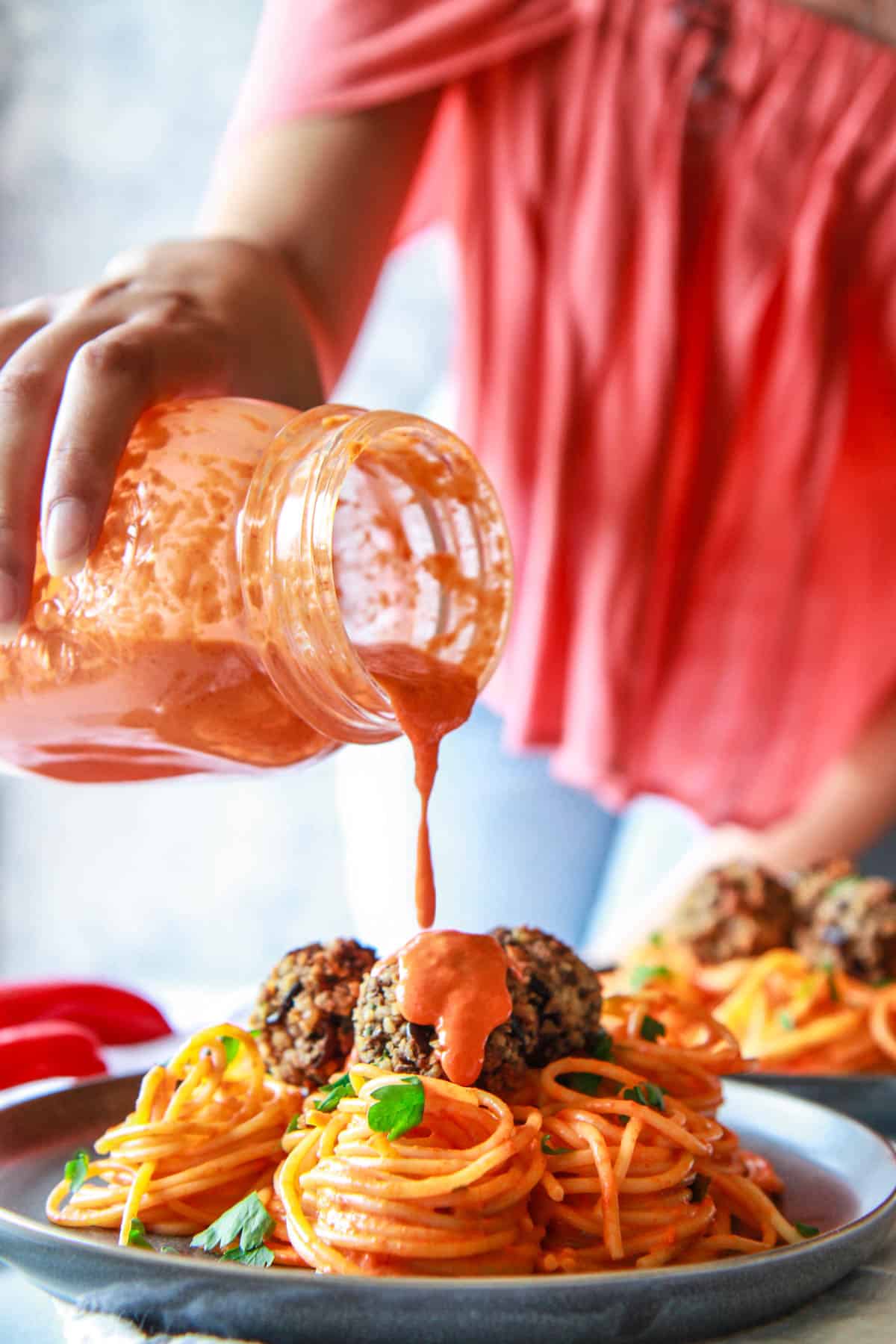 Pouring roasted red pepper sauce over the eggplant meatballs and pasta.