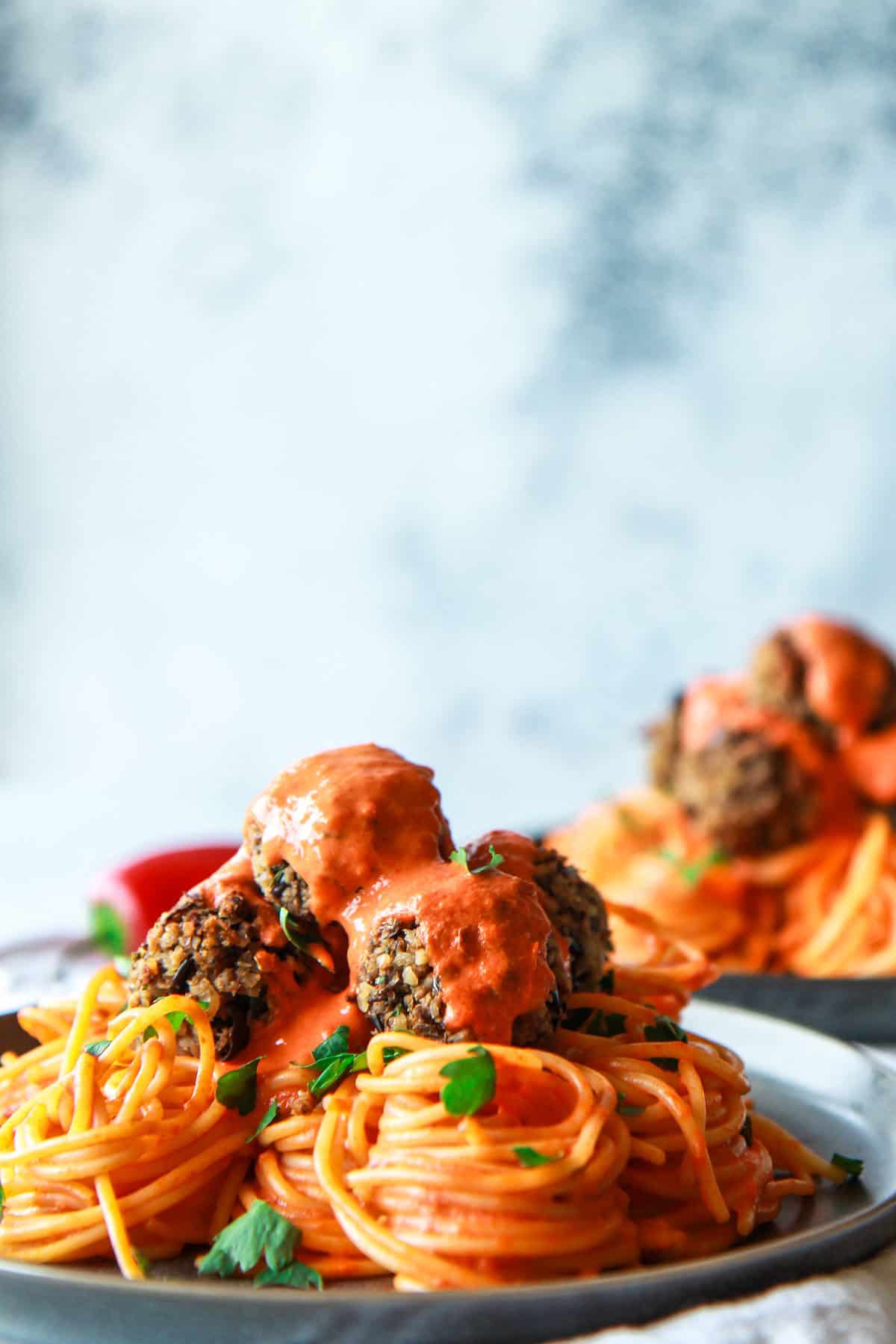 How the vegan baked eggplant meatballs look topped with roasted pepper sauce, served over pasta, from a head-on angle.