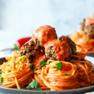 Vegan baked eggplant meatballs topped with roasted pepper sauce, served over pasta.