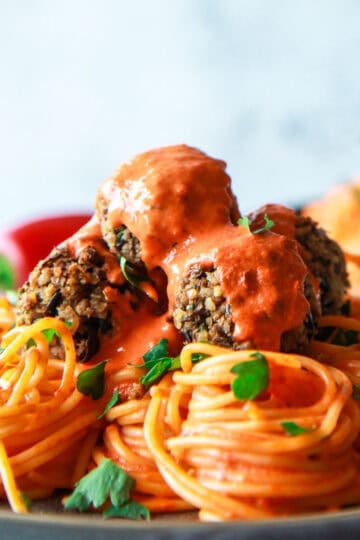 Vegan baked eggplant meatballs topped with roasted pepper sauce, served over pasta.