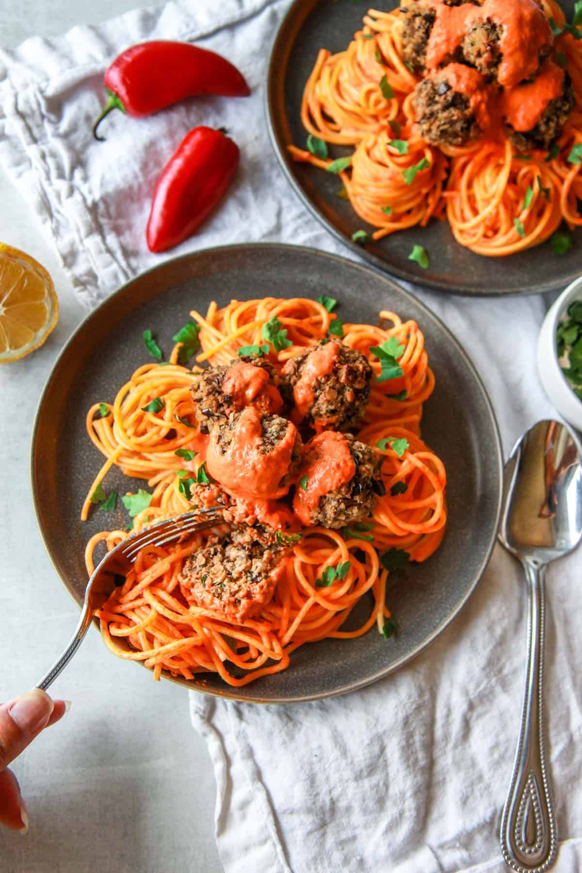 The eggplant meatballs are plated over pasta, showing the texture inside of one of the baked eggplant meatballs.