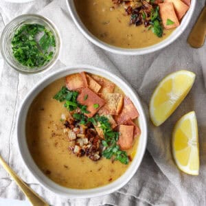A bowl of Arabic lentil soup topped with pita chips, crispy onions, and parsley, and served with lemon.