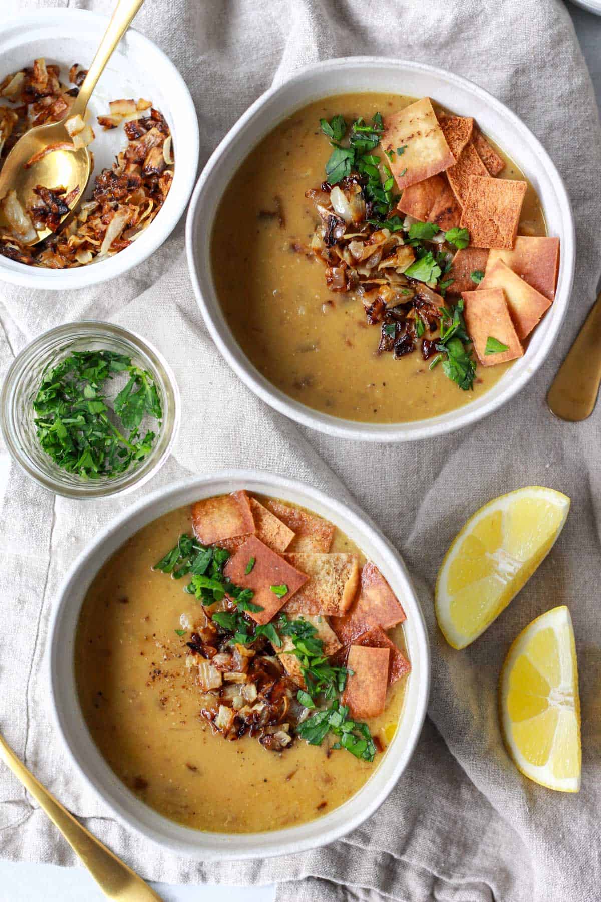 Two bowls of Syrian lentil soup served with crispy onions, parsley, and lemon.