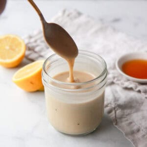 Drizzling the maple tahini dressing with a spoon to show the texture, with the image cropped square.