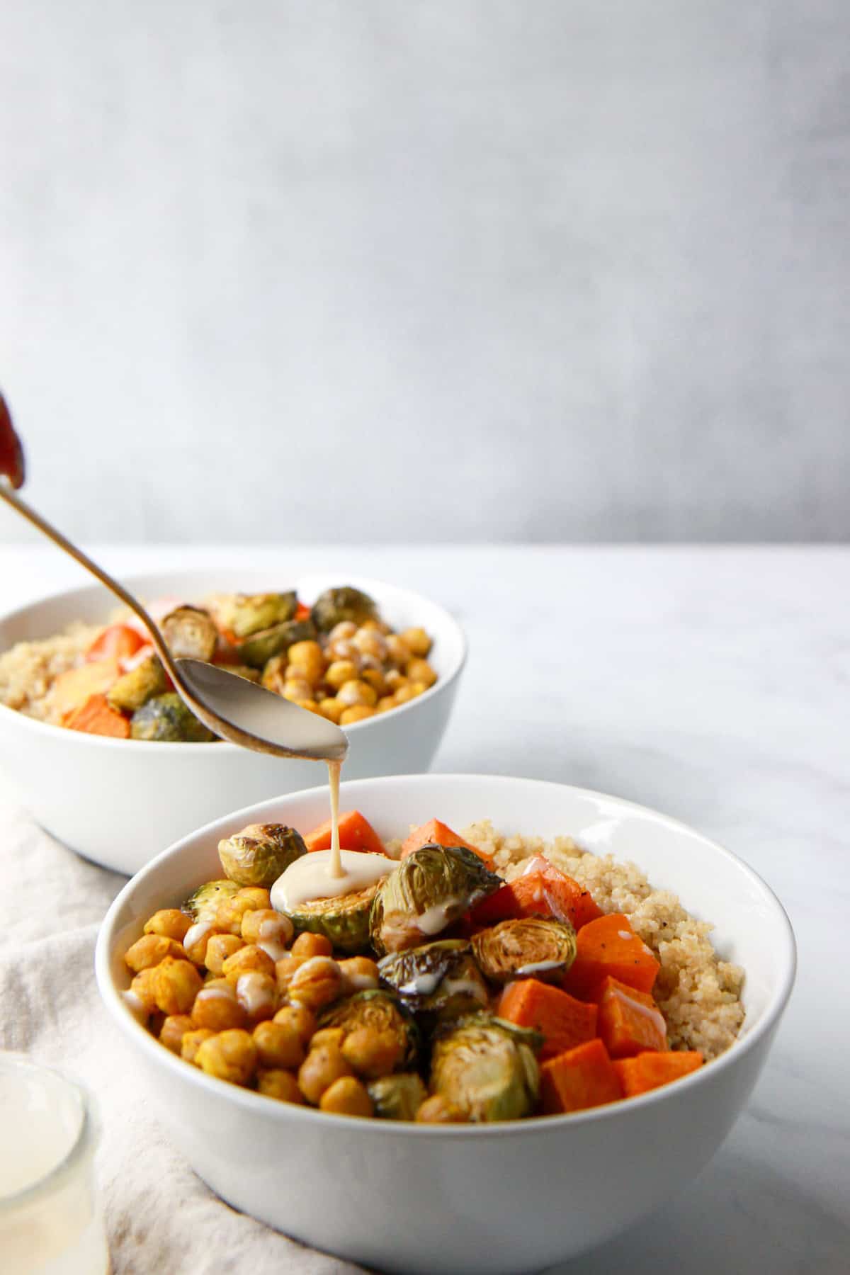 Pouring the maple tahini dressing over grain bowls.