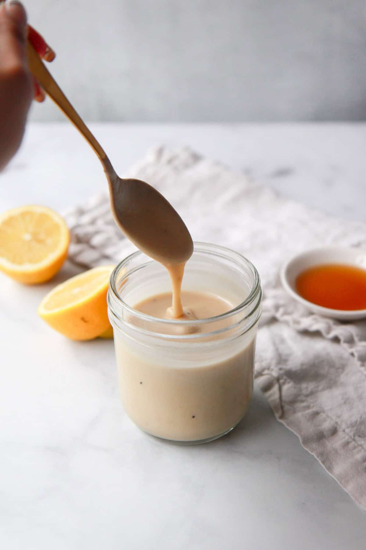 Drizzling the maple tahini dressing with a spoon to show the texture.