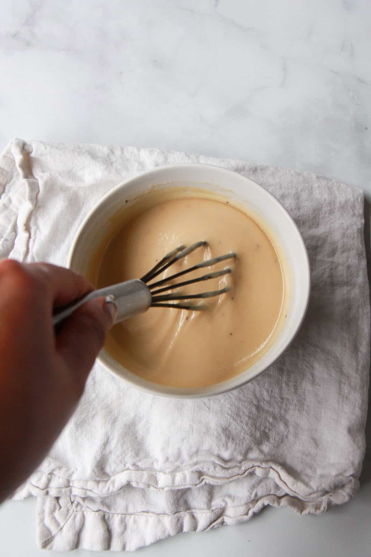 Thinning the maple tahini dressing with water and adding salt and pepper.