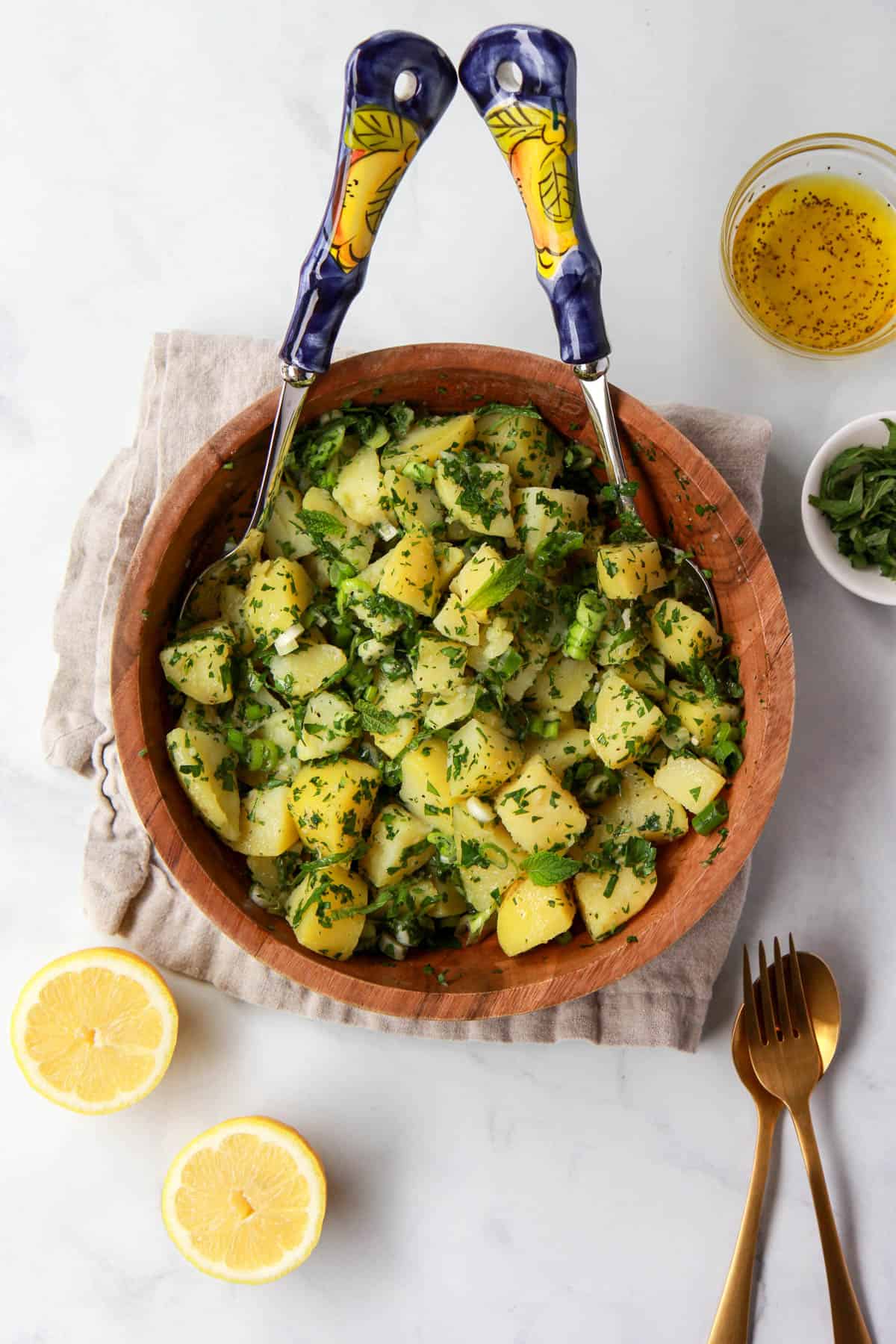 Hero flatlay image of Mediterranean potato salad, showing lemon and herbs, and dressing on the side.