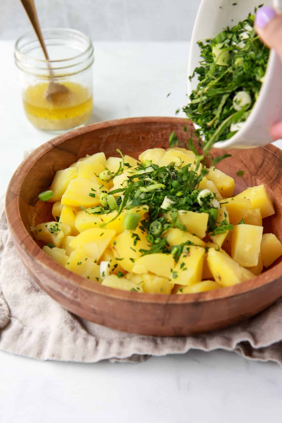 Pouring herbs over Syrian potato salad.