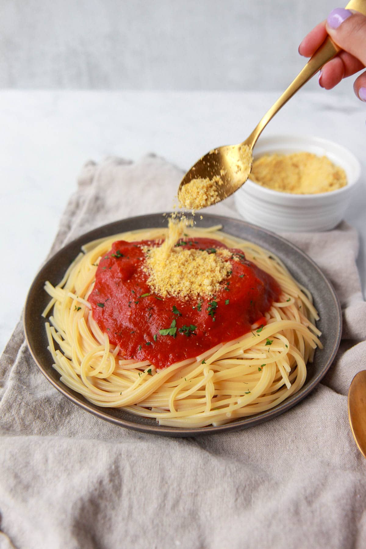 Almond parmesan being sprinkled over a plate of spaghetti with tomato sauce.