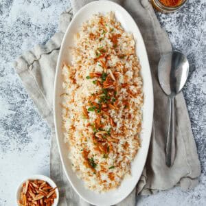 Flatlay image of finished vermicelli rice topped with toasted almonds and parsley, cropped square.