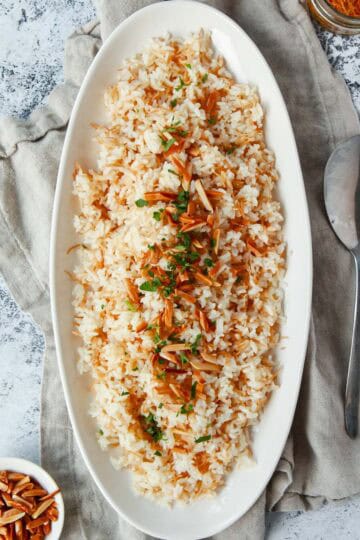 Flatlay image of finished vermicelli rice topped with toasted almonds and parsley, cropped square.