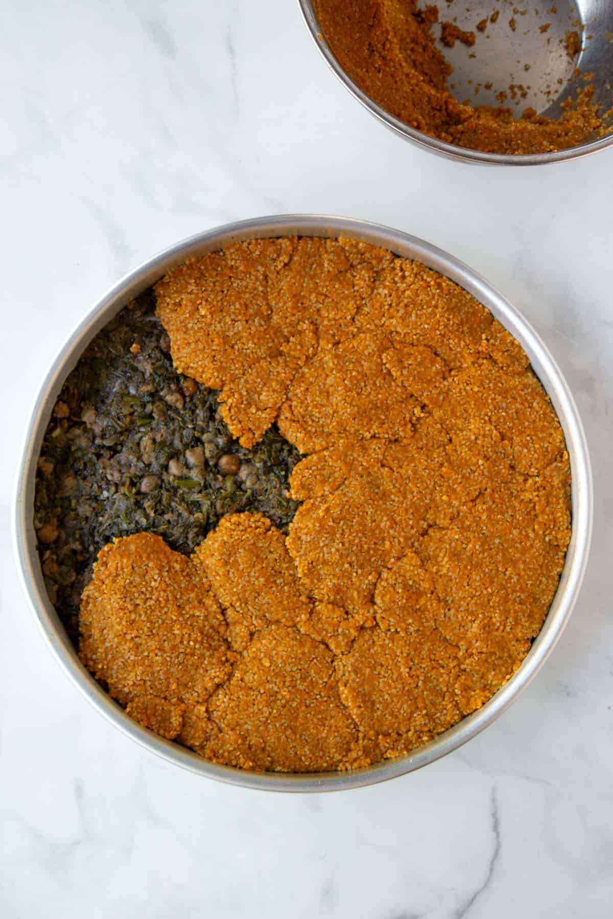 Placing the top layer of pumpkin bulgur dough on top of the filling.