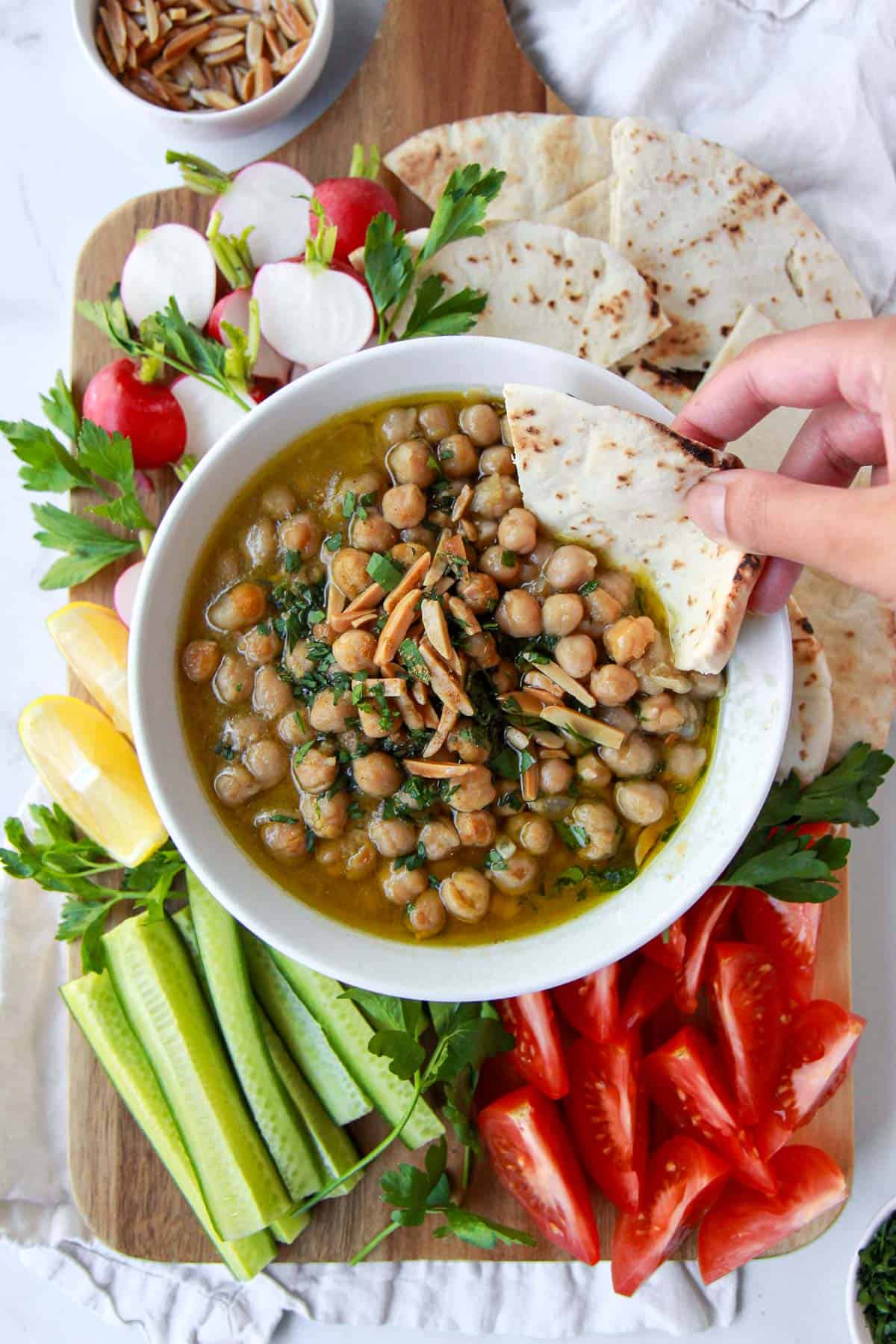Finished balila chickpeas being scooped up with pita bread and served with fresh veggies.