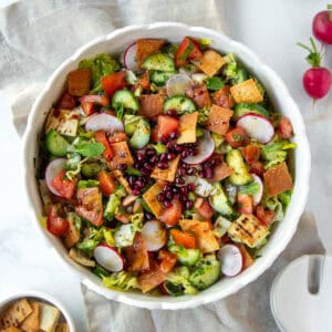 Fattoush salad with radishes, cucumbers, tomatoes, and crispy pita chips in a white bowl.