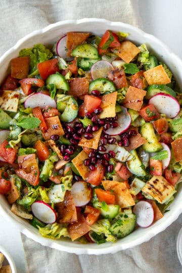 Fattoush salad with radishes, cucumbers, tomatoes, and crispy pita chips in a white bowl.