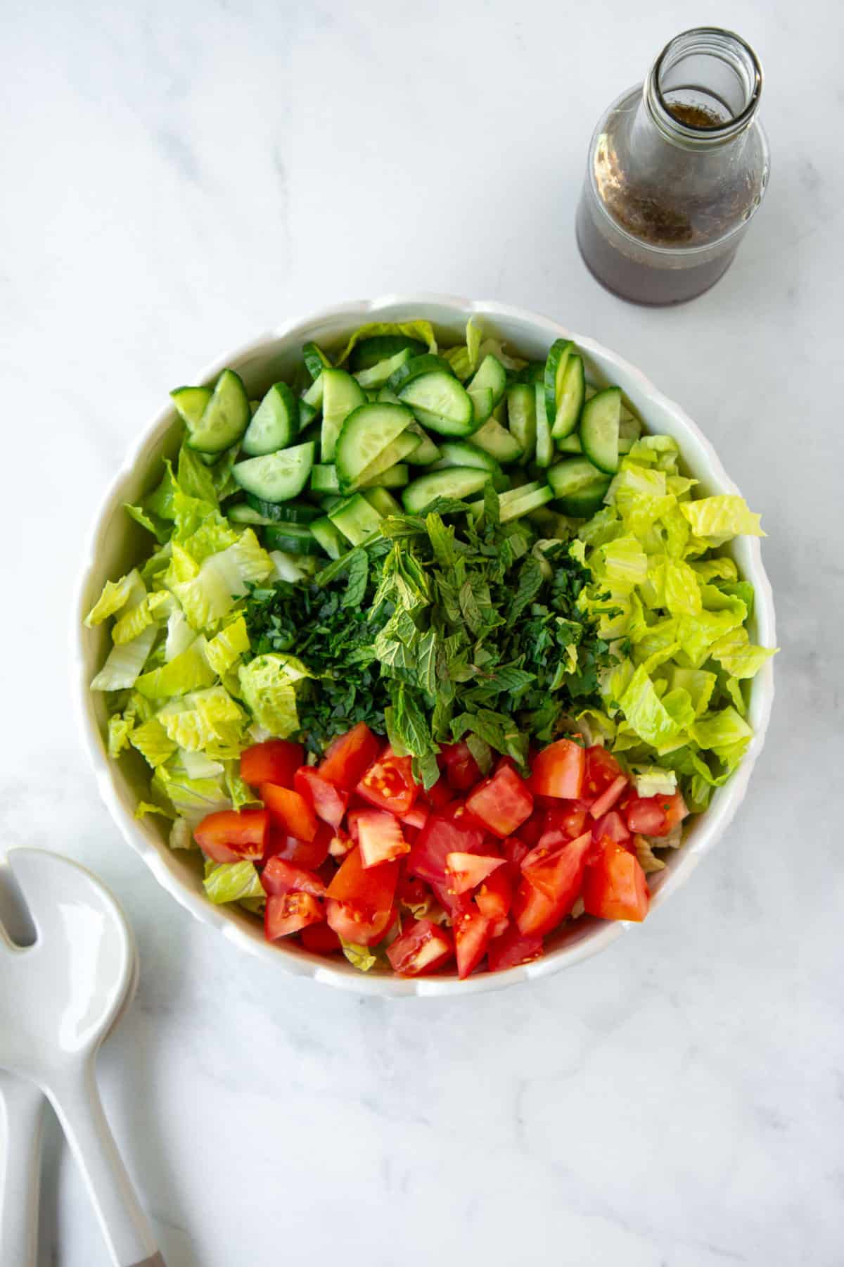 Fresh vegetable salad with cucumbers, tomatoes, lettuce, and herbs, on a white marble surface.