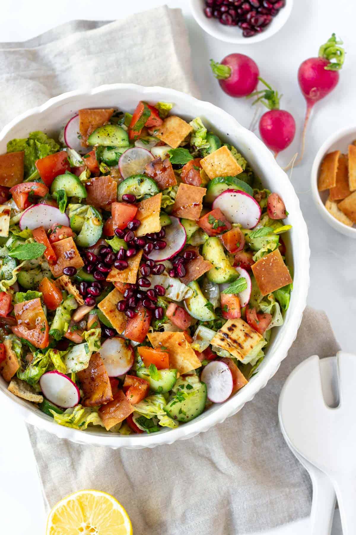 Fattoush salad with radishes, pomegranate seeds, and crispy pita chips in a white bowl, close up image showing texture.